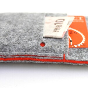 May include: A gray felt wallet with an orange trim and a small pocket for cash or cards. The wallet has the word "bholsa" printed on the front.
