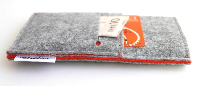 May include: A gray felt wallet with an orange trim and a small pocket for cash or cards. The wallet has the word "bholsa" printed on the front.