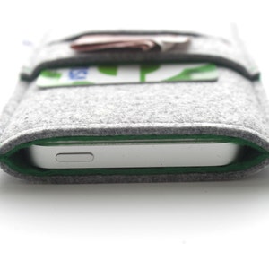 May include: A gray felt phone case with a green trim. The case has a pocket on the front for cards.