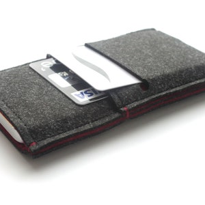 May include: A gray felt phone case with a red stitched edge. A credit card is tucked into the case's pocket.