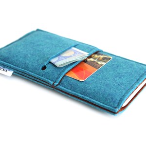 May include: A teal felt phone case with brown stitching and a small pocket for cards and cash. The case has a white label with the word "shalsu" printed on it.