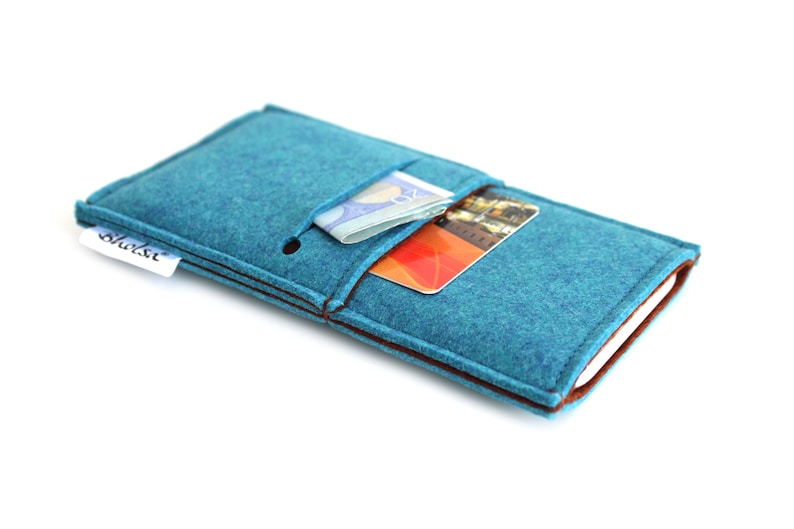 May include: A teal felt phone case with brown stitching and a small pocket for cards and cash. The case has a white label with the word "shalsu" printed on it.