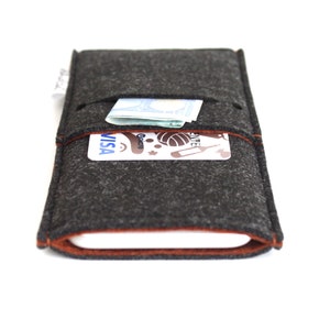 May include: A gray felt phone case with a brown felt trim. The case has a pocket on the back for a credit card or cash. The case is shown with a credit card and cash inside the pocket.