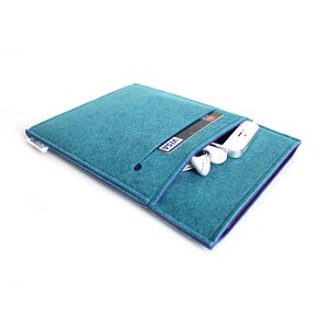 May include: Teal felt tablet sleeve with a purple trim and a zippered pocket. The pocket contains a credit card and a pair of white earbuds.