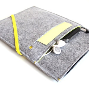 Peut inclure: Pochette en feutre gris avec une sangle jaune et une poche jaune. La pochette contient un smartphone, des écouteurs et un stylet.