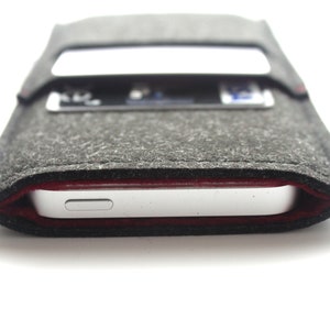 May include: A gray felt phone case with a red stitch detail. The case has a slot for a credit card or ID card.