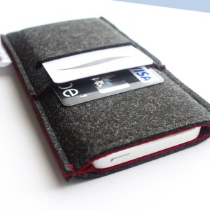 May include: A gray felt phone case with a red stitched edge. The case has a pocket on the back for holding cards. The case is shown with a credit card and a debit card in the pocket.
