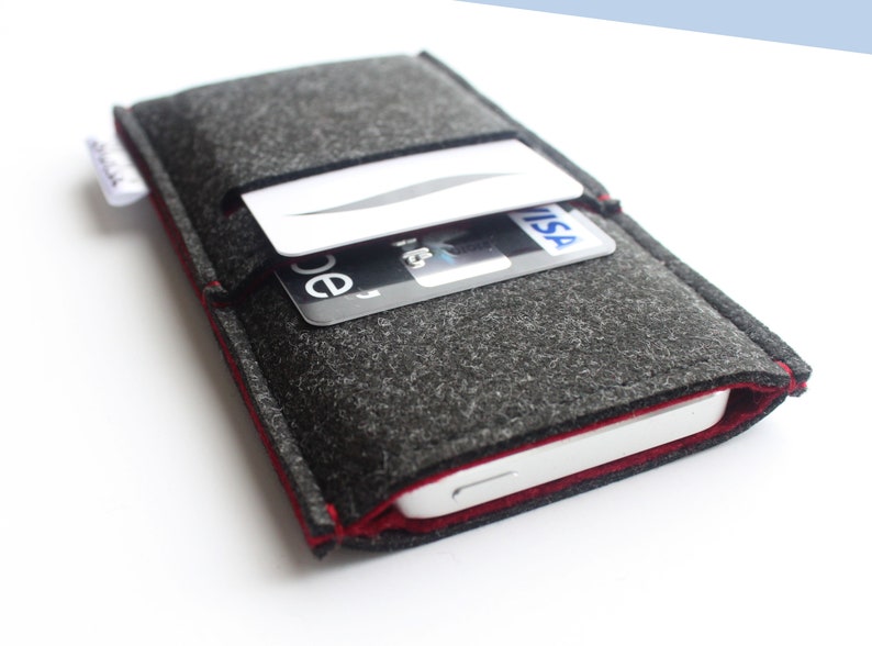May include: A gray felt phone case with a red stitched edge. The case has a pocket on the back for holding cards. The case is shown with a credit card and a debit card in the pocket.