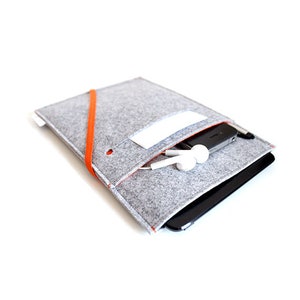 May include: A gray felt sleeve with an orange elastic band and a white label. The sleeve is designed to hold a tablet or phone and has a pocket for headphones.