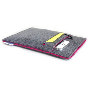 May include: Gray felt sleeve with a hot pink trim and a yellow accent. The sleeve has a black drawstring closure and a small white tag. A silver smartphone is partially visible inside the sleeve.