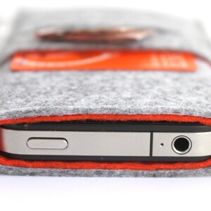 May include: A gray felt phone case with an orange stitched border. The case is designed to fit a smartphone and has a small pocket on the back.