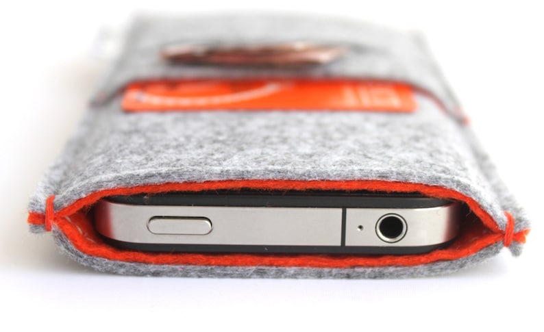 May include: A gray felt phone case with an orange stitched border. The case is designed to fit a smartphone and has a small pocket on the back.