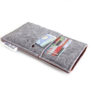 May include: Gray felt phone case with a brown felt trim. The case has a pocket for cards and cash. The case has a small white label with the word "bholsi" on it.