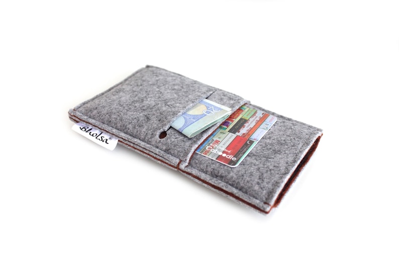 May include: Gray felt phone case with a brown felt trim. The case has a pocket for cards and cash. The case has a small white label with the word "bholsi" on it.
