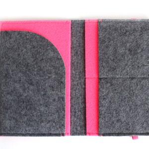 Può includere: Un portafoglio in feltro grigio con un interno in feltro rosa. Il portafoglio ha più tasche e una tasca curva sul lato sinistro. Il portafoglio è etichettato "BholSa" nell'angolo in basso a destra.