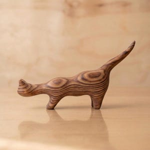 May include: A wooden cat figurine with a striped pattern in shades of brown. The cat is in a standing pose with its tail raised. The figurine is carved from wood and has a smooth finish.