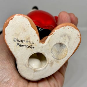 Puede incluir: Una figurita de cer&aacute;mica de Mickey Mouse con un atuendo rojo y negro. La figurita est&aacute; de pie sobre sus pies y tiene un agujero en la parte inferior. La parte inferior de la figurita est&aacute; marcada con el texto "&copy; WALT DISNEY PRODUCTION".