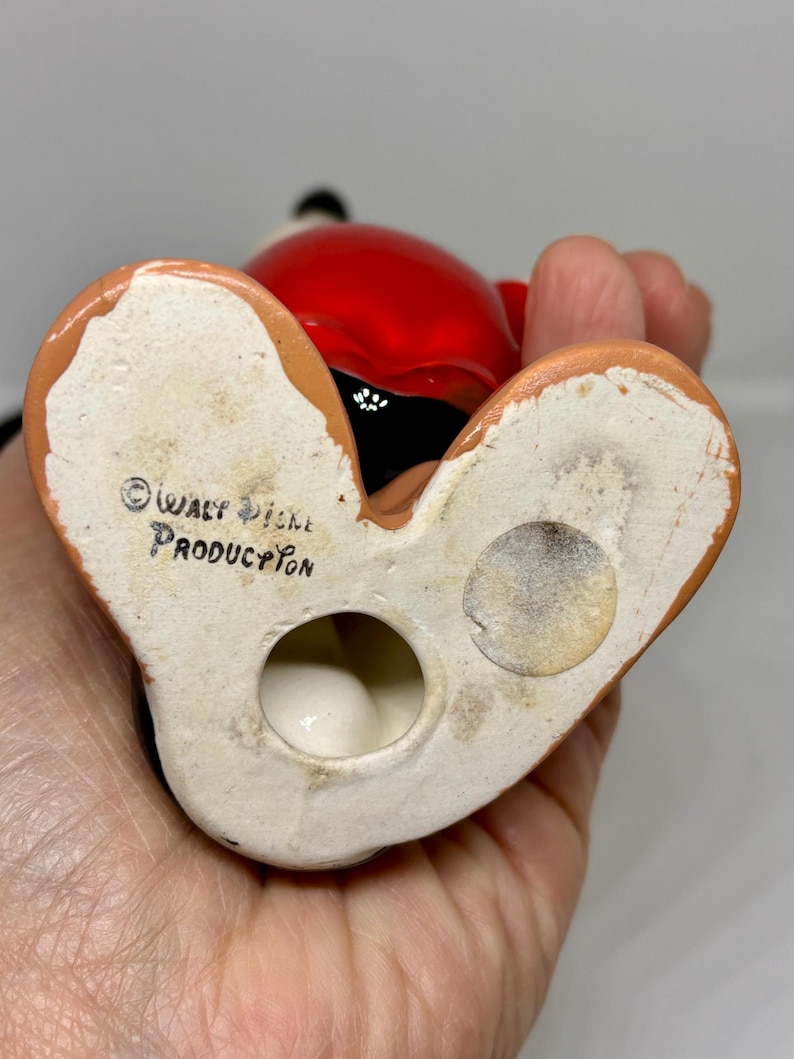 Puede incluir: Una figurita de cer&aacute;mica de Mickey Mouse con un atuendo rojo y negro. La figurita est&aacute; de pie sobre sus pies y tiene un agujero en la parte inferior. La parte inferior de la figurita est&aacute; marcada con el texto "&copy; WALT DISNEY PRODUCTION".