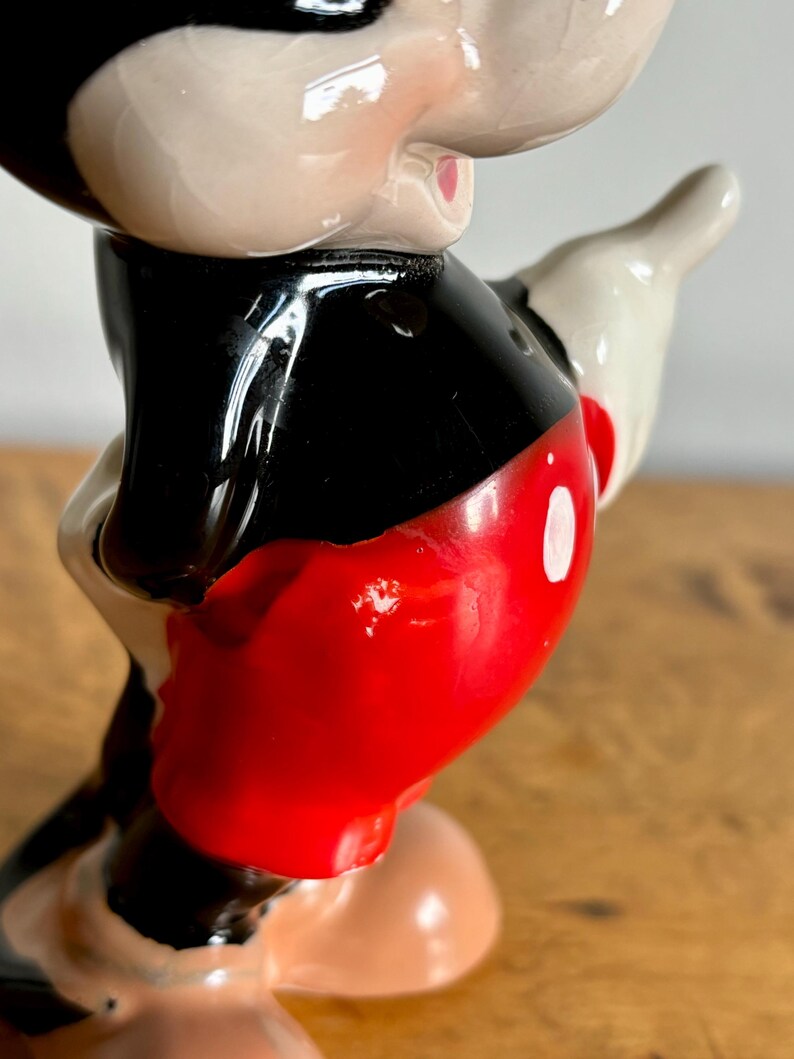 Puede incluir: Una figurita de cer&aacute;mica de Mickey Mouse. Lleva sus caracter&iacute;sticos pantalones cortos rojos con un c&iacute;rculo blanco, zapatos negros y guantes blancos. Su rostro est&aacute; pintado con ojos negros, una nariz roja y una amplia sonrisa.
