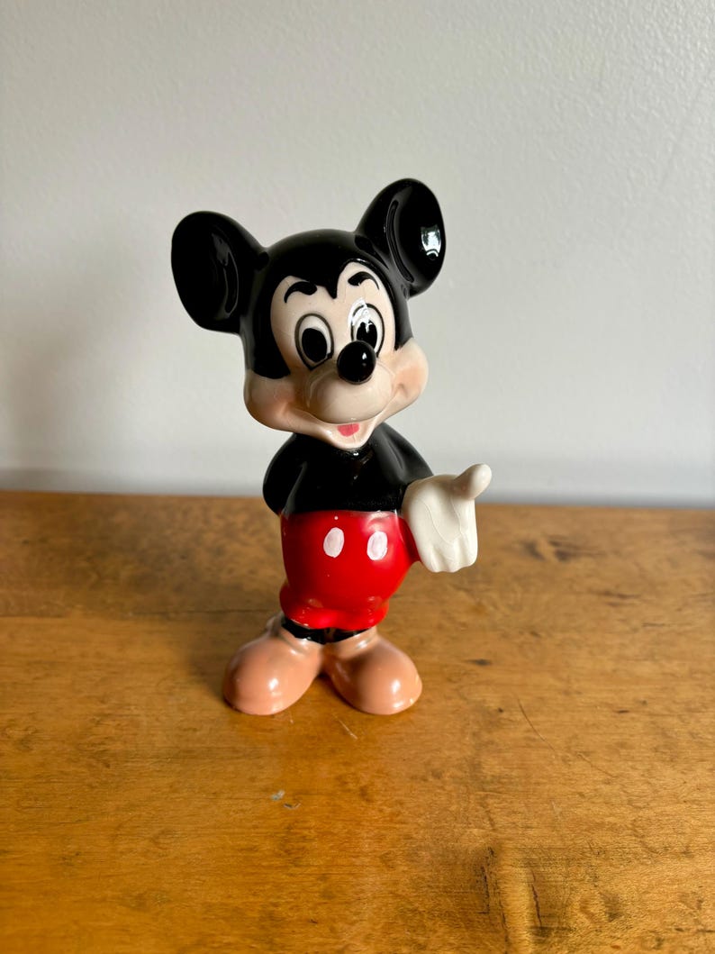 Puede incluir: Una figurita de cer&aacute;mica negra y blanca de Mickey Mouse. Mickey lleva sus pantalones cortos rojos caracter&iacute;sticos con dos botones blancos y guantes blancos. Est&aacute; sonriendo y tiene una nariz negra y orejas grandes negras.