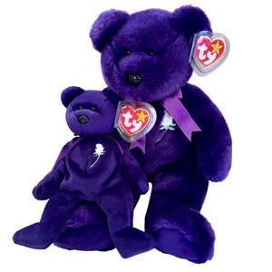 May include: Two plush purple teddy bears. The larger bear has a purple ribbon around its neck and a white rose embroidered on its chest. Both bears have the Ty heart-shaped tag attached. The bears are on a white background.