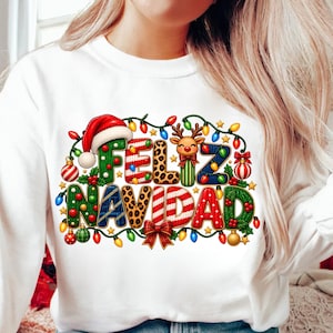 May include: A white long-sleeve sweatshirt featuring a colourful graphic print that reads "FELIZ NAVIDAD" in decorative, patterned letters. The design includes a Santa hat, a reindeer, Christmas lights, ornaments, and a red bow.