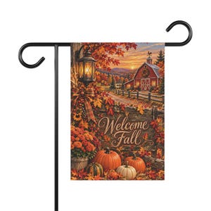 Puede incluir: Una bandera de jardín rectangular colgada en un soporte de metal negro, con una escena otoñal impresa que muestra un granero rojo, calabazas naranjas, follaje, un farol encendido y el texto Welcome Fall sobre un fondo de valla de madera.