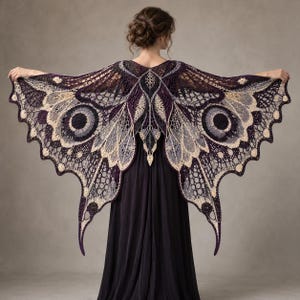 May include: A dark purple and cream crochet shawl shaped like large butterfly wings with intricate openwork patterns, circular eye-like motifs, and scalloped edges, worn over a solid dark purple floor-length dress.