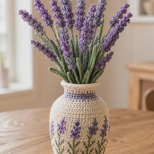 May include: A crochet vase in cream with a lavender floral pattern, containing a bouquet of crocheted lavender stems. The stems feature textured purple flower spikes and green leaves, while the vase has a matching purple band at the neck.