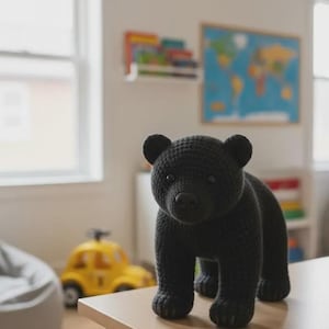 May include: A black crocheted bear toy with a textured yarn surface, rounded ears, and dark plastic eyes. The bear is standing on all four legs, featuring a detailed snout and paws, crafted with a consistent stitch pattern throughout its body.