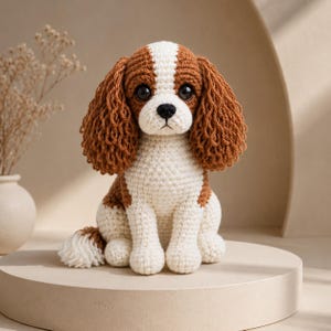 Peut inclure: Une peluche crochetée représentant un chien Cavalier King Charles Spaniel. Le jouet présente un motif en fil blanc et marron, de longues oreilles texturées, un nez noir et de grands yeux sombres, assis en position verticale.