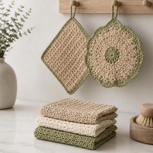 May include: Two crocheted pot holders in diamond and circular shapes, featuring beige and sage green yarn, hang from a wooden rack. Below, a stack of three folded crocheted washcloths in beige, cream, and sage green sits on a flat surface.