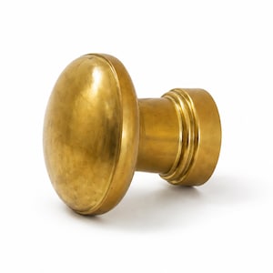 May include: A polished brass door knob featuring a smooth, rounded front face and a cylindrical base with two distinct horizontal ridges. The metal surface has a warm, golden metallic finish with subtle variations in tone across the curved shape.