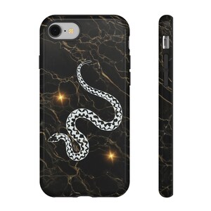 May include: A black phone case with a gold marble pattern and a white snake illustration. The design features a central white snake with a geometric pattern on its back, set against a dark background with gold veining and two small starbursts.