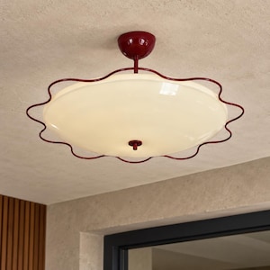 May include: A ceiling light fixture featuring a large, circular, off-white glass shade held by a deep red metal frame with a wavy, scalloped edge. The fixture includes a matching deep red canopy and a central red knob securing the glass shade.