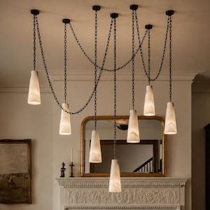 May include: A multi-pendant chandelier featuring seven conical, white marble-patterned shades suspended by dark metal chains. The chains are draped in a swag style from the ceiling, creating a cascading arrangement of illuminated light fixtures.