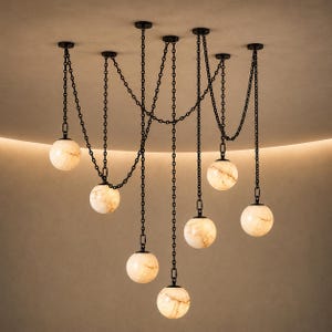 May include: A multi-light chandelier featuring seven spherical, cream-colored stone globes suspended at varying heights. Each globe is attached to a black metal chain that connects to the ceiling, creating a draped, interconnected web design.