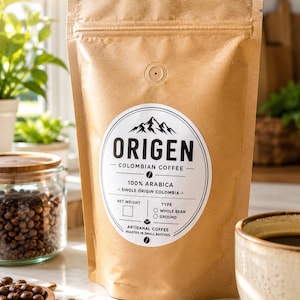 May include: A brown paper coffee bag with a white circular label featuring the text Origen, Colombian Coffee, 100% Arabica, Single Origin Colombia, and Artisanal Coffee Roasted in Small Batches, with a degassing valve at the top center.