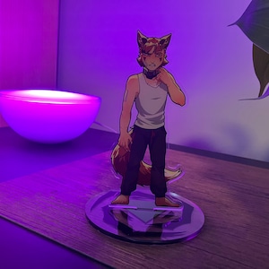 May include: A clear acrylic figure of a fox-like character in a white tank top and black pants, standing on a circular base. The figure has brown fur and ears, with a tail. The background features a purple-lit lamp and a plant.