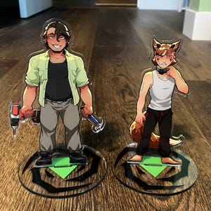 May include: Two acrylic standees featuring cartoon characters. One holds a drill and hammer, wearing a green shirt, black shirt, and gray pants. The other is a fox-like character in a white tank top and black pants. Both stand on circular bases.