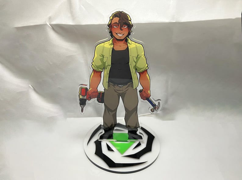 Op de afbeelding: Een acryl figuur in cartoonstijl van een persoon met een boor en een hamer. De figuur draagt een geel overhemd over een zwart shirt, een bruine broek en zwarte laarzen. Het staat op een wit en zwarte cirkelvormige basis met een groene pijl.