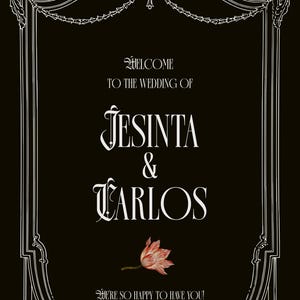 May include: A black rectangular wedding sign with a white ornate border. The text reads: WELCOME TO THE WEDDING OF JESINTA & CARLOS. A single pink and white flower is centered below the names, followed by the text: WE'RE SO HAPPY TO HAVE YOU!