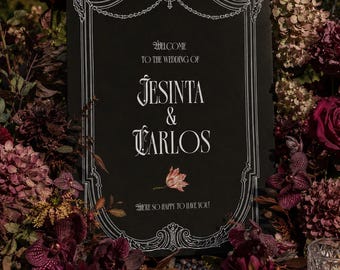 May include: A rectangular black wedding sign with white decorative border detailing and text reading Welcome to the wedding of Jesinta & Carlos, with a small floral illustration and the text We're so happy to have you printed below.