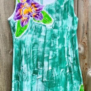 Peut inclure: Une robe sans manches avec un motif abstrait peint &agrave; la main en coups de pinceau verts. Le v&ecirc;tement pr&eacute;sente une grande fleur d'orchid&eacute;e violette et jaune sur le haut de la poitrine gauche et des feuilles vertes sur l'ourlet inf&eacute;rieur droit.