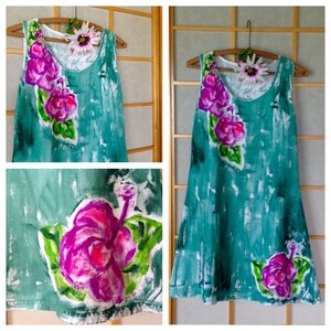 Peut inclure: Une robe sans manches de couleur vert sarcelle avec un effet peint &agrave; la main pr&eacute;sentant des textures de coups de pinceau blancs. La robe est orn&eacute;e de motifs de fleurs d'hibiscus magenta et violet vif avec des feuilles vertes sur l'&eacute;paule et l'ourlet.