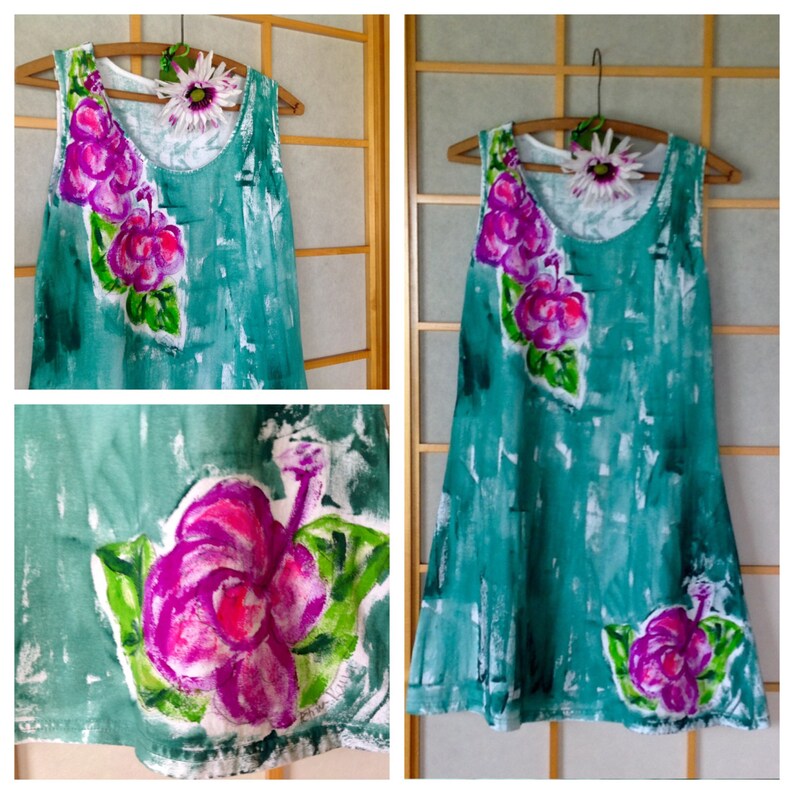 Peut inclure: Une robe sans manches de couleur vert sarcelle avec un effet peint &agrave; la main pr&eacute;sentant des textures de coups de pinceau blancs. La robe est orn&eacute;e de motifs de fleurs d'hibiscus magenta et violet vif avec des feuilles vertes sur l'&eacute;paule et l'ourlet.