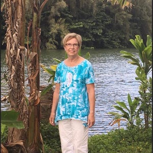 May include: A short-sleeved tunic top featuring a vibrant blue and white abstract pattern with a central white feather graphic, paired with solid white cropped pants. The top has a rounded neckline and a slightly asymmetrical hemline.