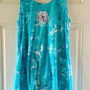 May include: A sleeveless tank top featuring a vibrant turquoise and white tie-dye pattern. The garment has a scoop neckline and a centered, circular graphic print of a dark blue ammonite fossil design on the upper chest area.