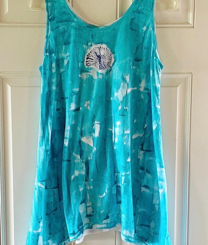 May include: A sleeveless tank top featuring a vibrant turquoise and white tie-dye pattern. The garment has a scoop neckline and a centered, circular graphic print of a dark blue ammonite fossil design on the upper chest area.