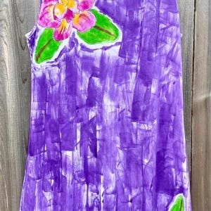 Peut inclure: Une robe sans manches avec un motif abstrait peint &agrave; la main en coups de pinceau violets. Le v&ecirc;tement pr&eacute;sente une grande fleur rose et jaune avec des feuilles vertes pr&egrave;s de l'encolure et une feuille verte pr&egrave;s de l'ourlet inf&eacute;rieur.